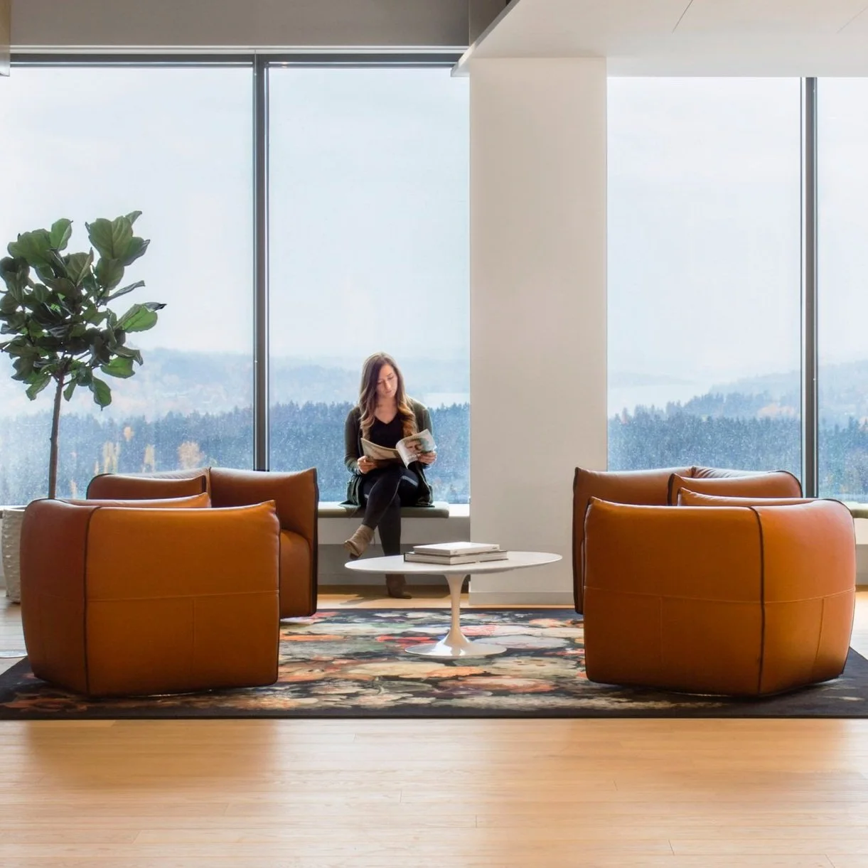 A sunlit workplace lounge with leather chairs, a white table and broad windows